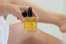 Elodie's Naturals: Body oil spray bottle beside a leg
