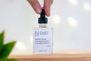 Elodie's Naturals: Hand holding the cap of a clear serum dropper bottle